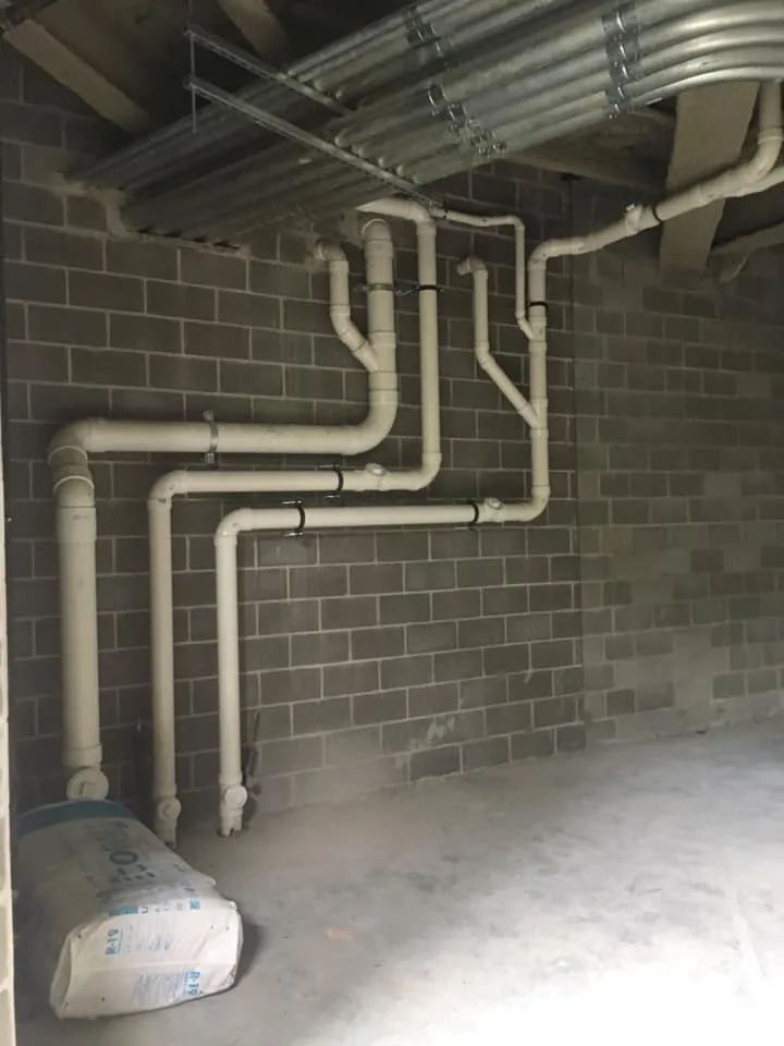 Drain piping run neatly along a painted block basement wall.