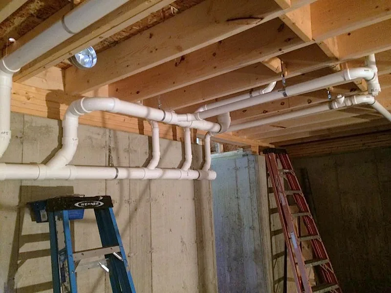 A supply run carried along a basement ceiling between joists with copper and plastic pipe.