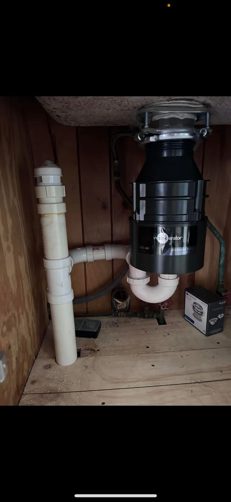 A garbage disposal unit mounted under a kitchen sink with its waste piping connected.