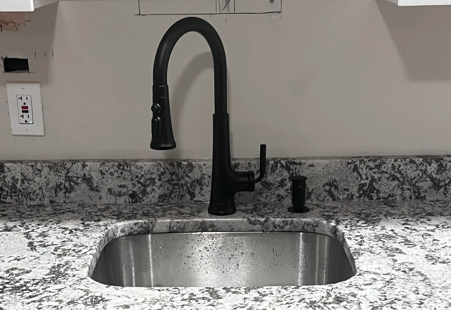 A black kitchen faucet installed over a stainless undermount sink in a granite worktop.