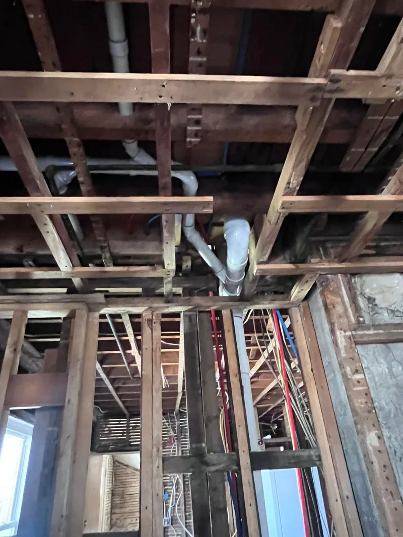 Pipework run overhead through floor joists in an unfinished ceiling.