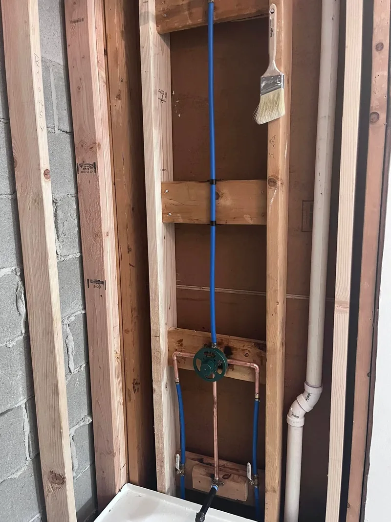 Supply lines run vertically through an open stud wall alongside copper pipe.