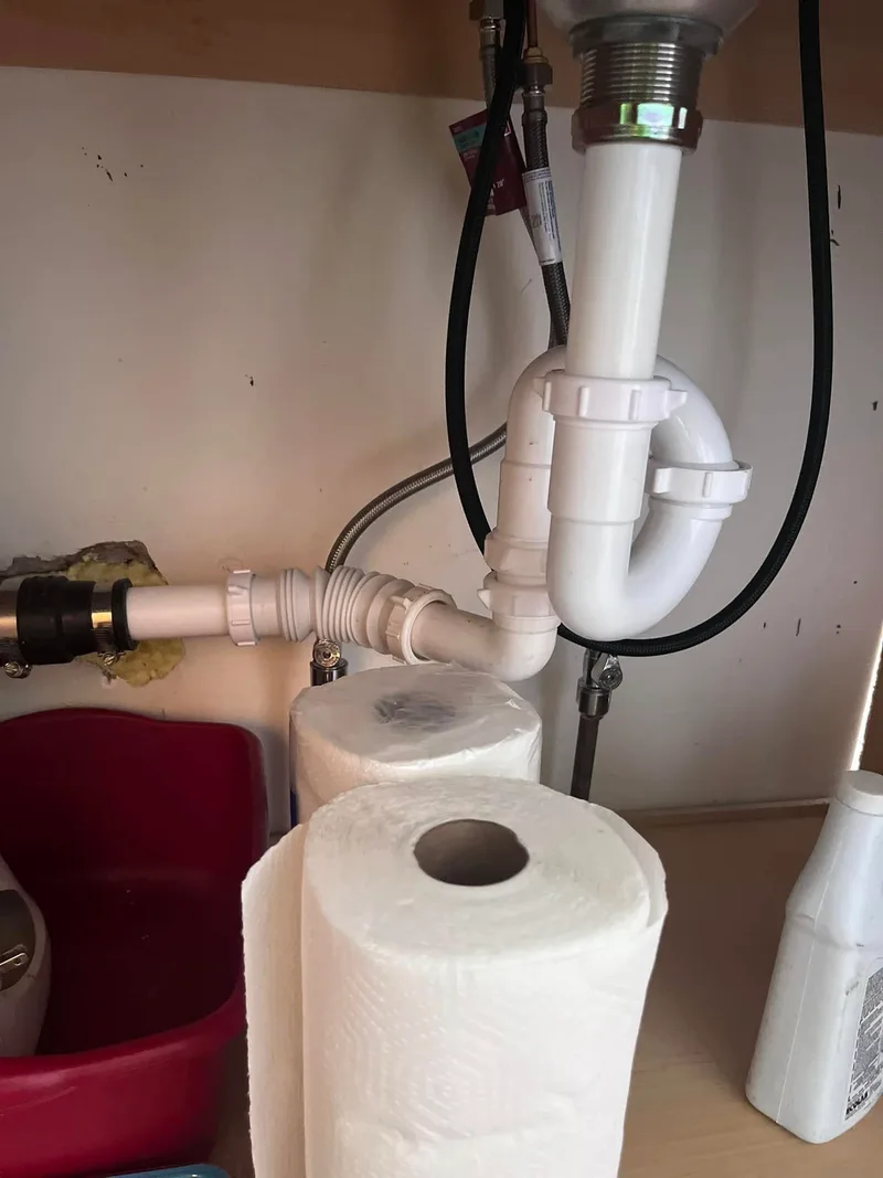 A second view of under-sink waste piping and a trap, seen from inside the cabinet.