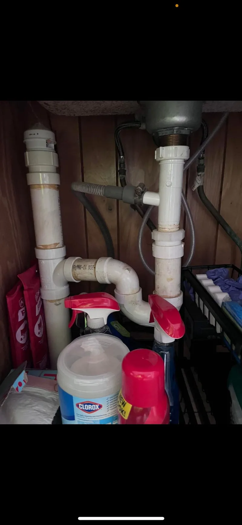 Waste piping and a trap fitted under a sink above stored household bottles.