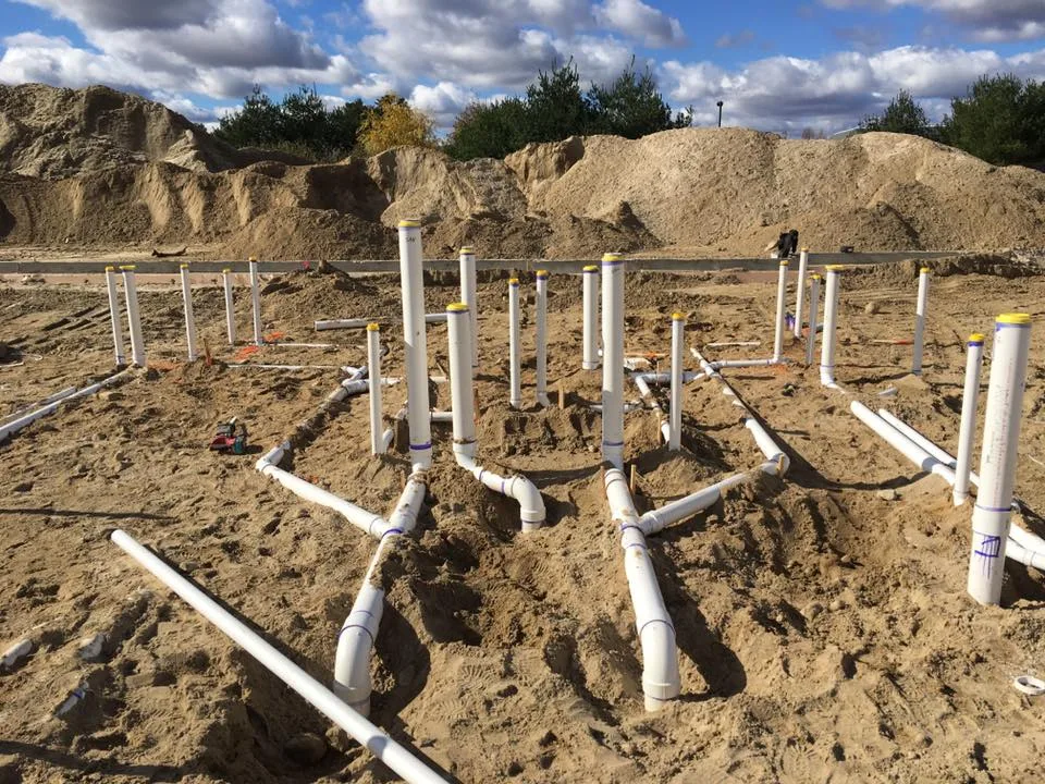 Underground drainage roughed in across a sand-bedded site with risers standing proud, under an open sky.