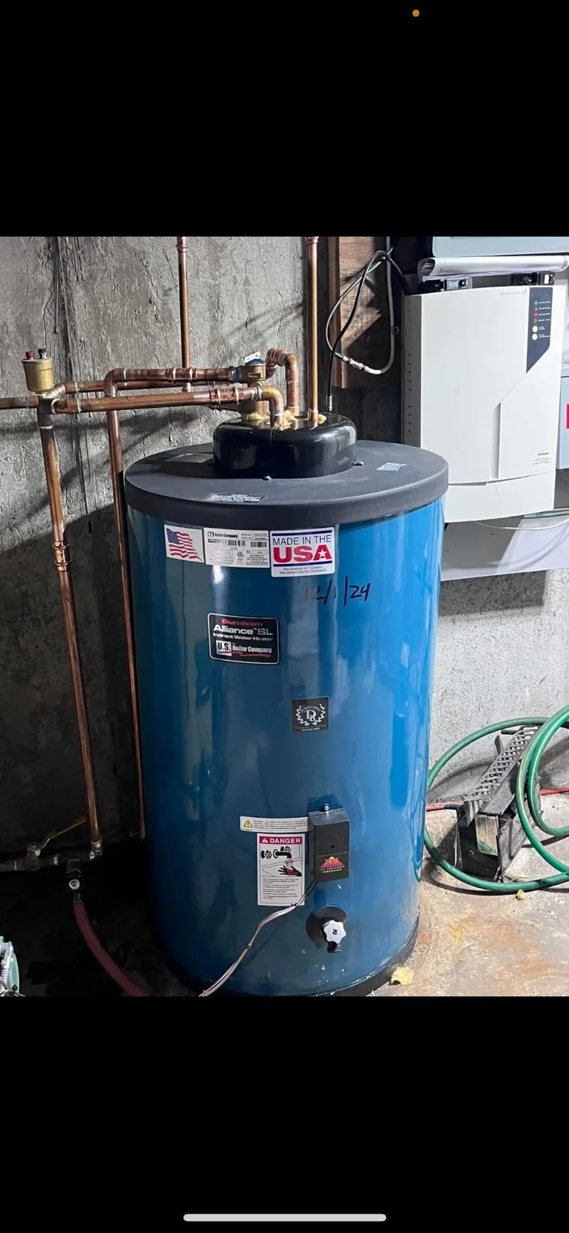 A water heater and adjacent tank in a basement, connected and running.