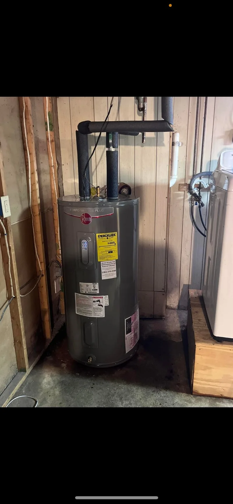 A newly installed water heater standing on a basement floor with its supply lines and venting connected.