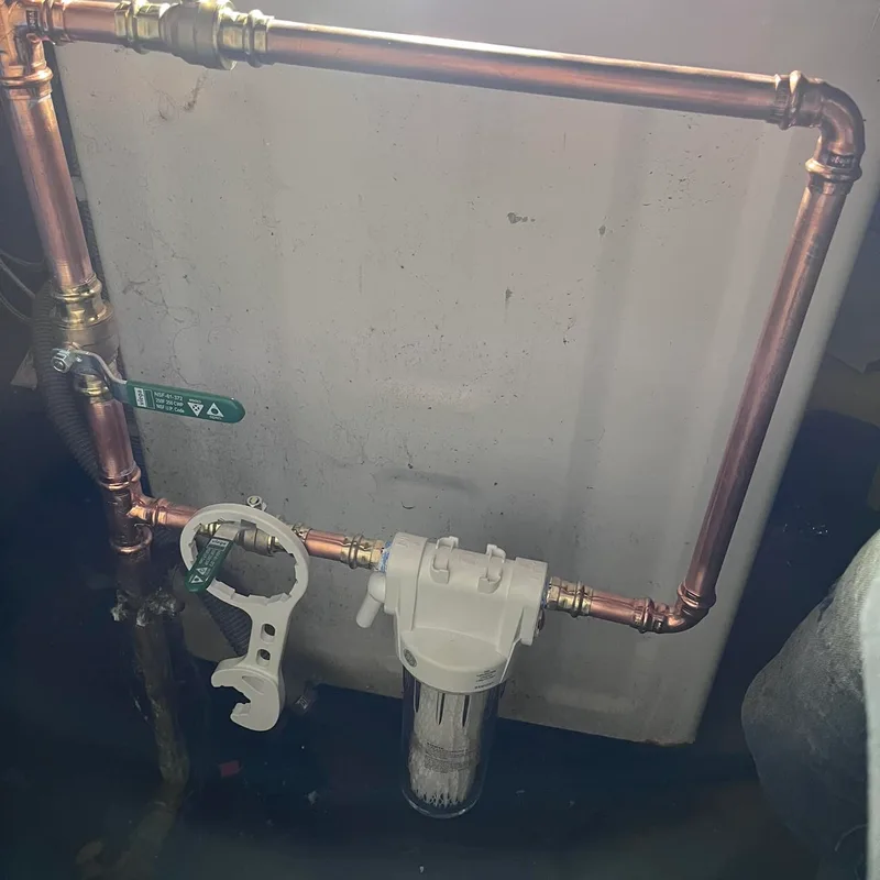 A whole-house water filter housing plumbed into a copper main with isolation valves either side.